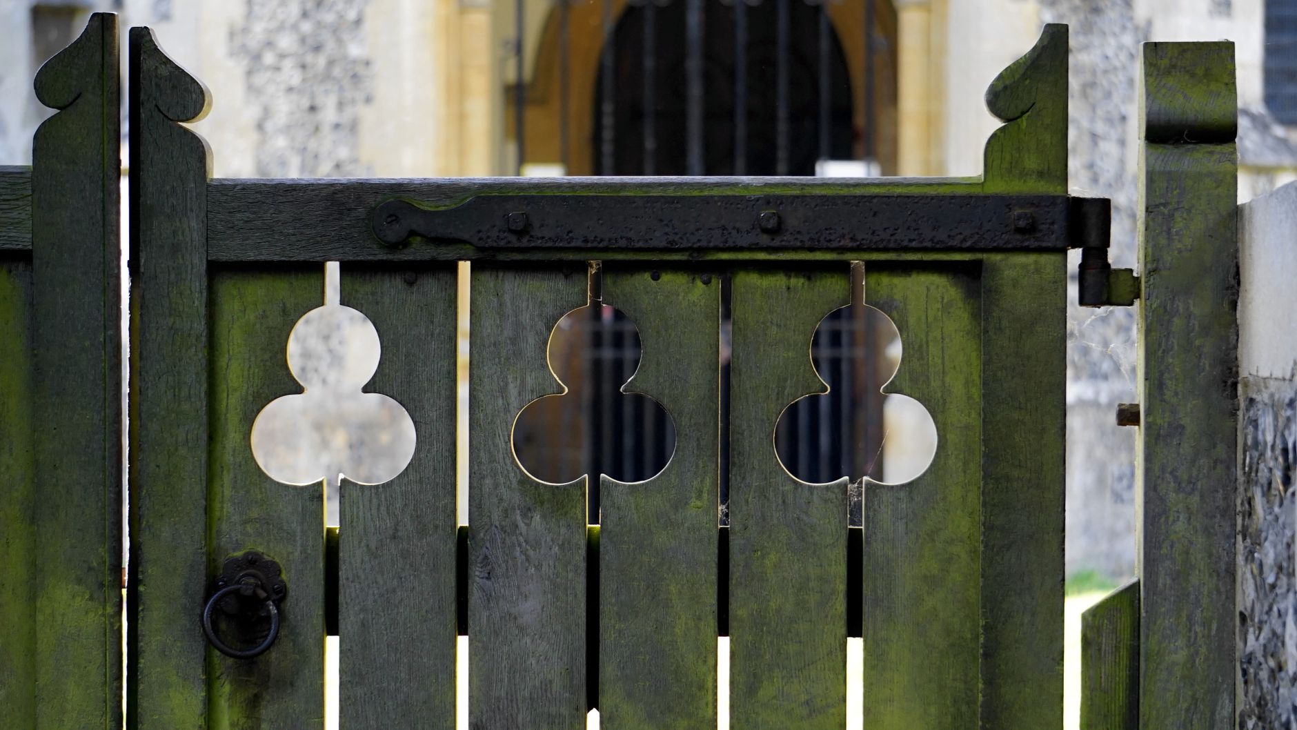Close-up of a rustic wooden gate with an ornate iron handle and green patina